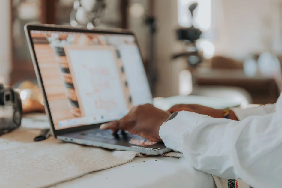 Hands using a tablet beside a laptop in a home office setting, showcasing online browsing.